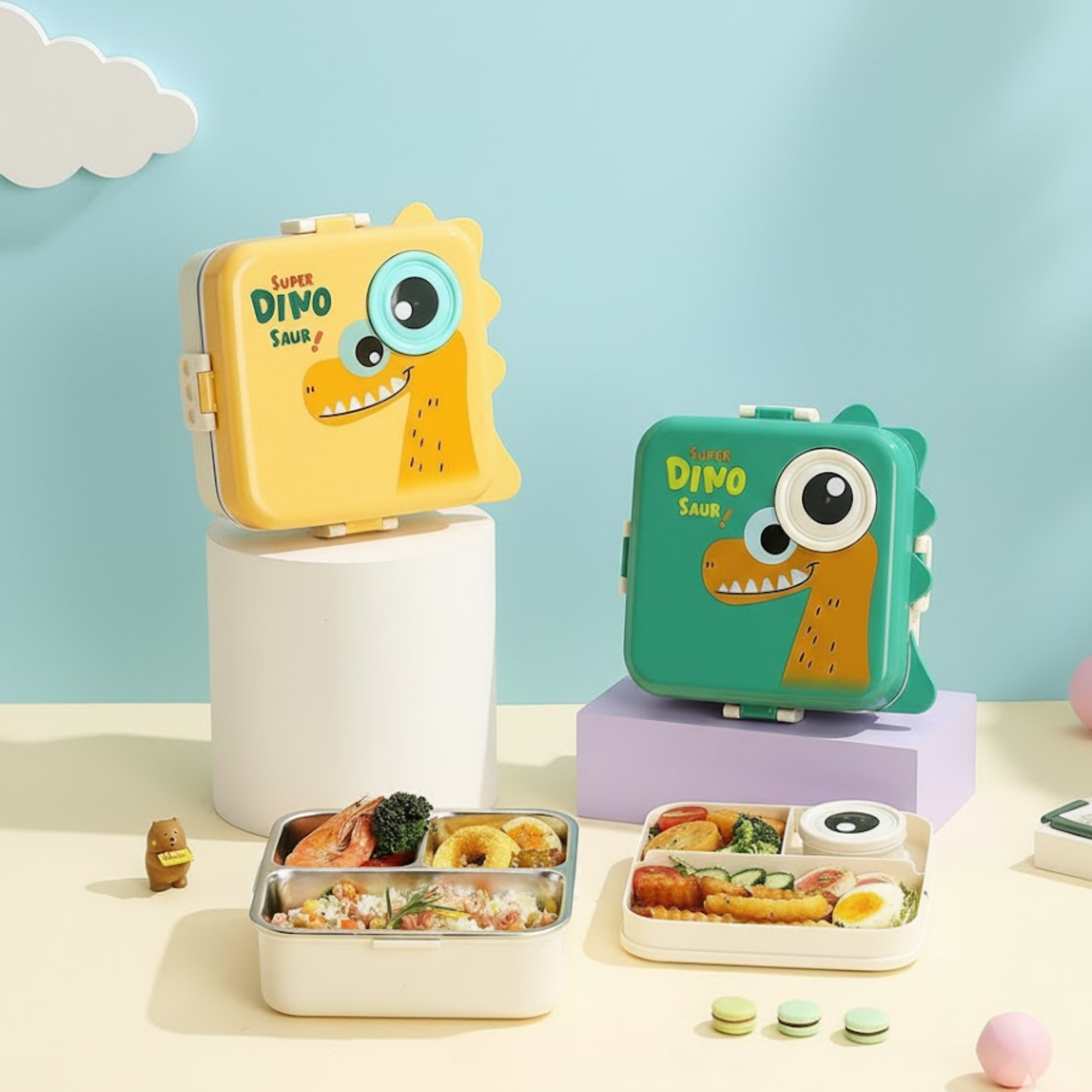Cute dinosaur-themed kids lunch boxes in yellow and green displayed with stainless steel food trays filled with meals 